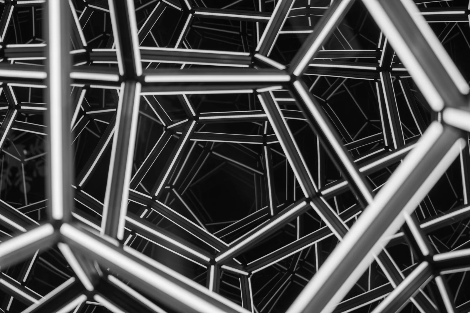 Black-and-white intersecting metal beams form a dense geometric structure.