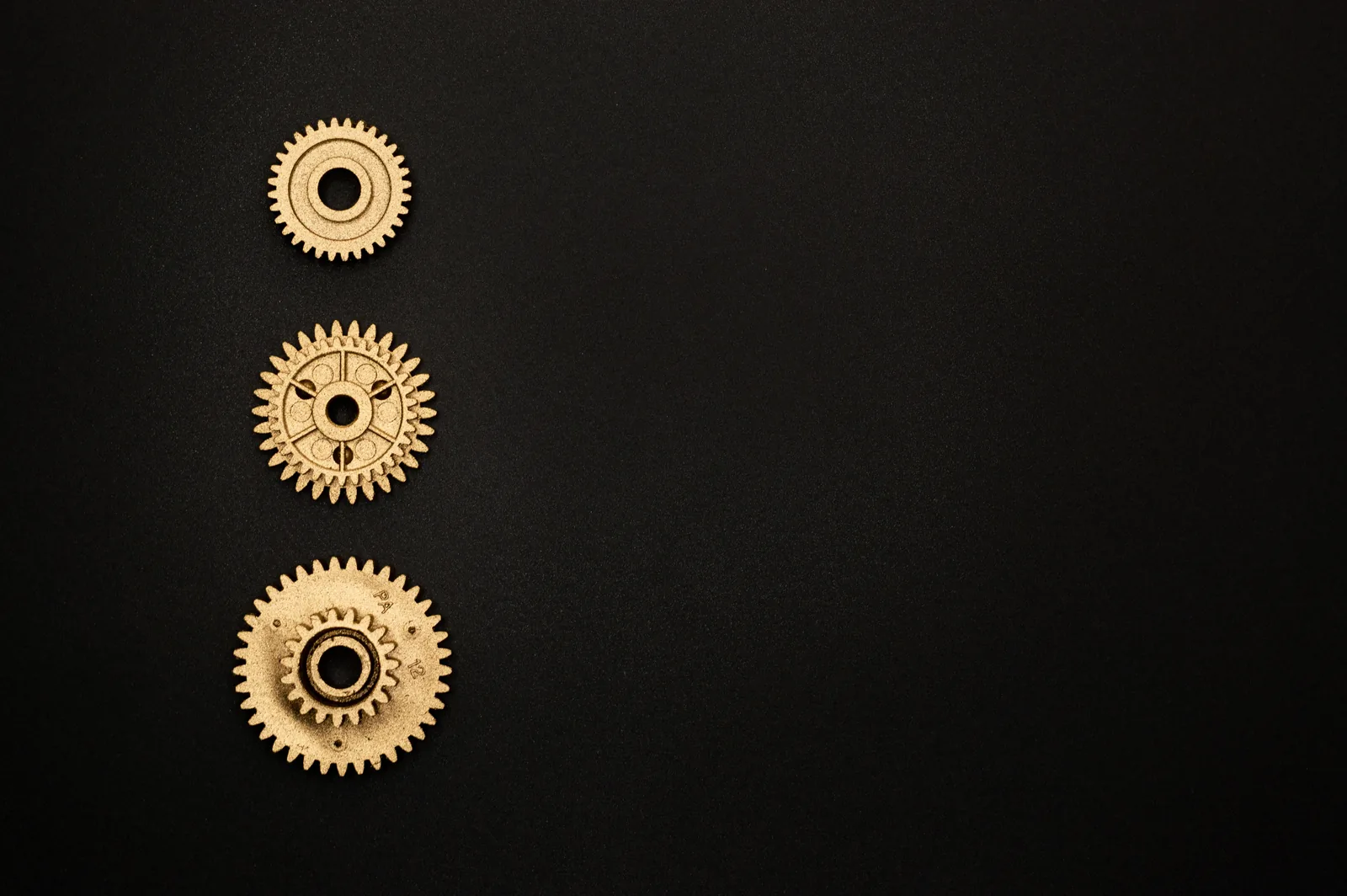 Three golden gears aligned vertically on a black surface