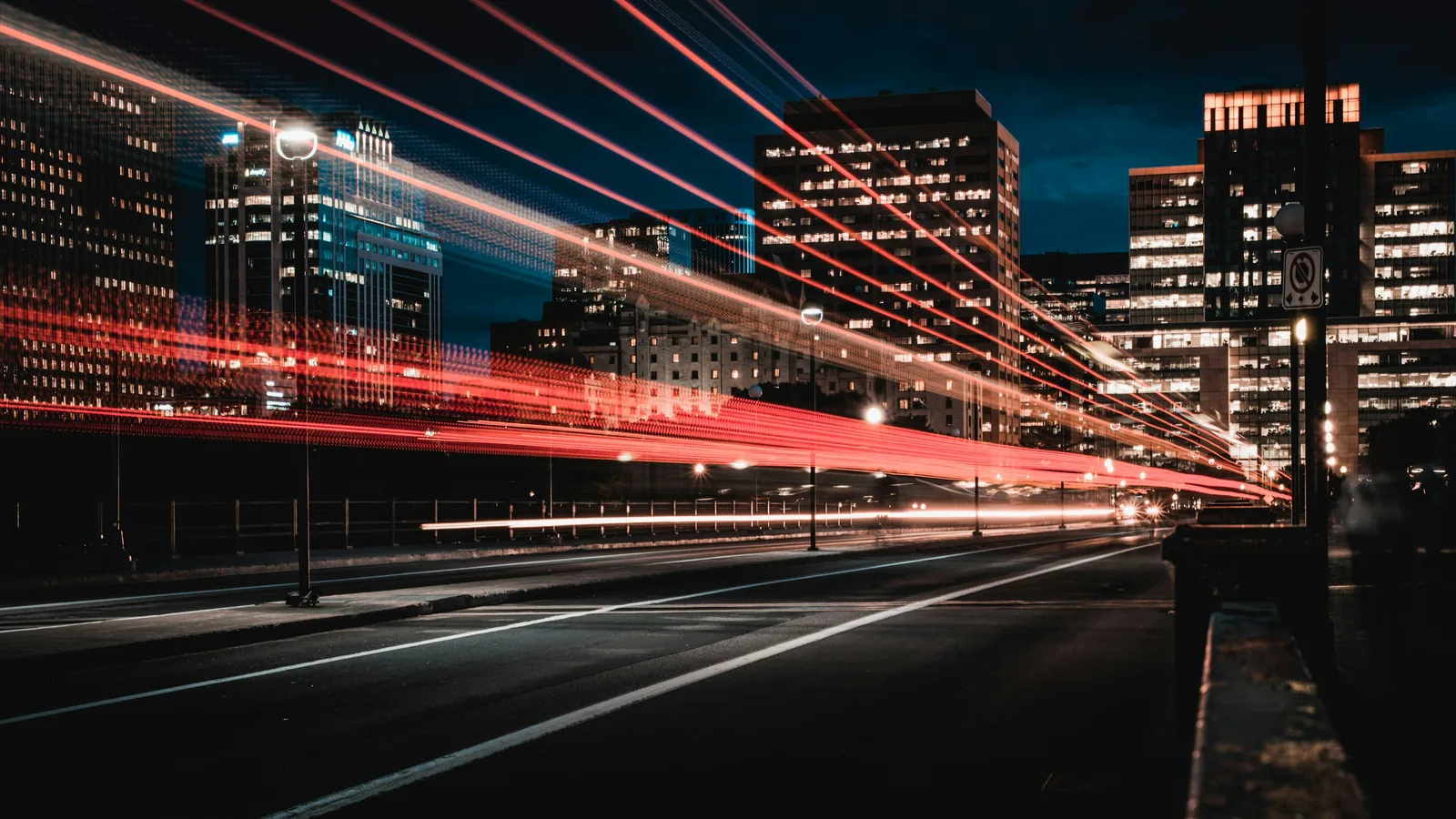 Red and white light trails stream past dark city buildings at night.