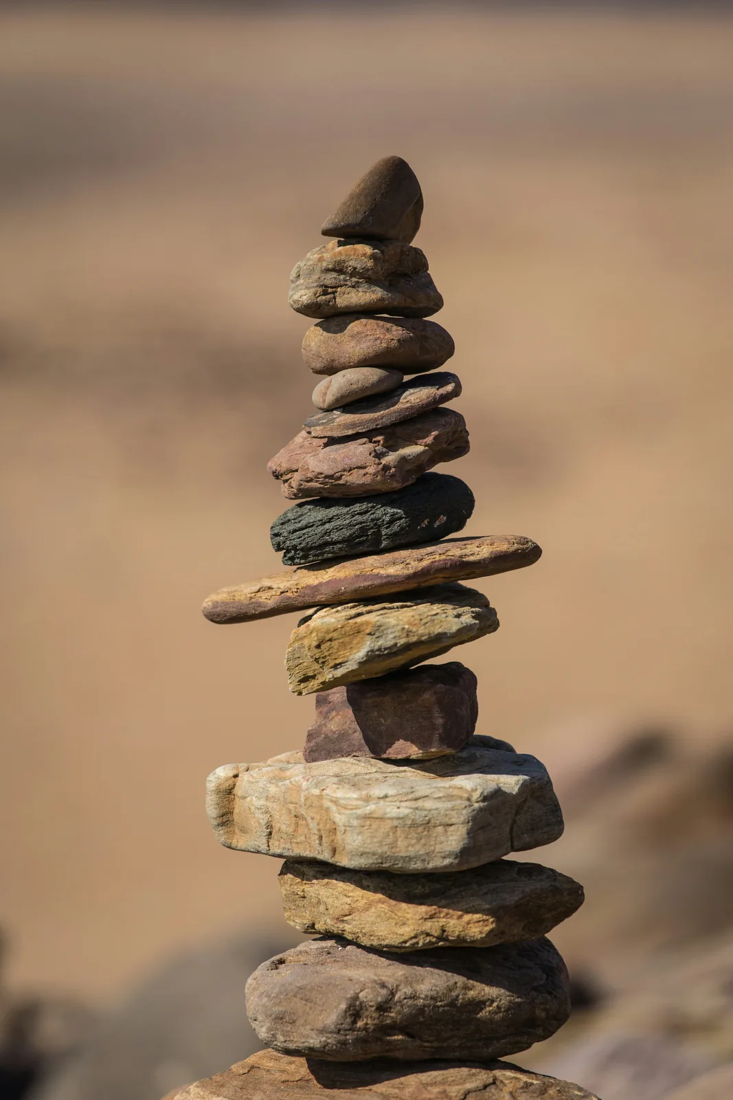 Seven smooth stones balanced in a vertical stack against a softly blurred background.